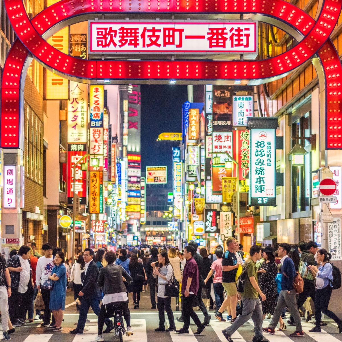 Belebte Einkaufsstraße mit leuchtenden Reklametafeln und vielen Passanten bei Nacht