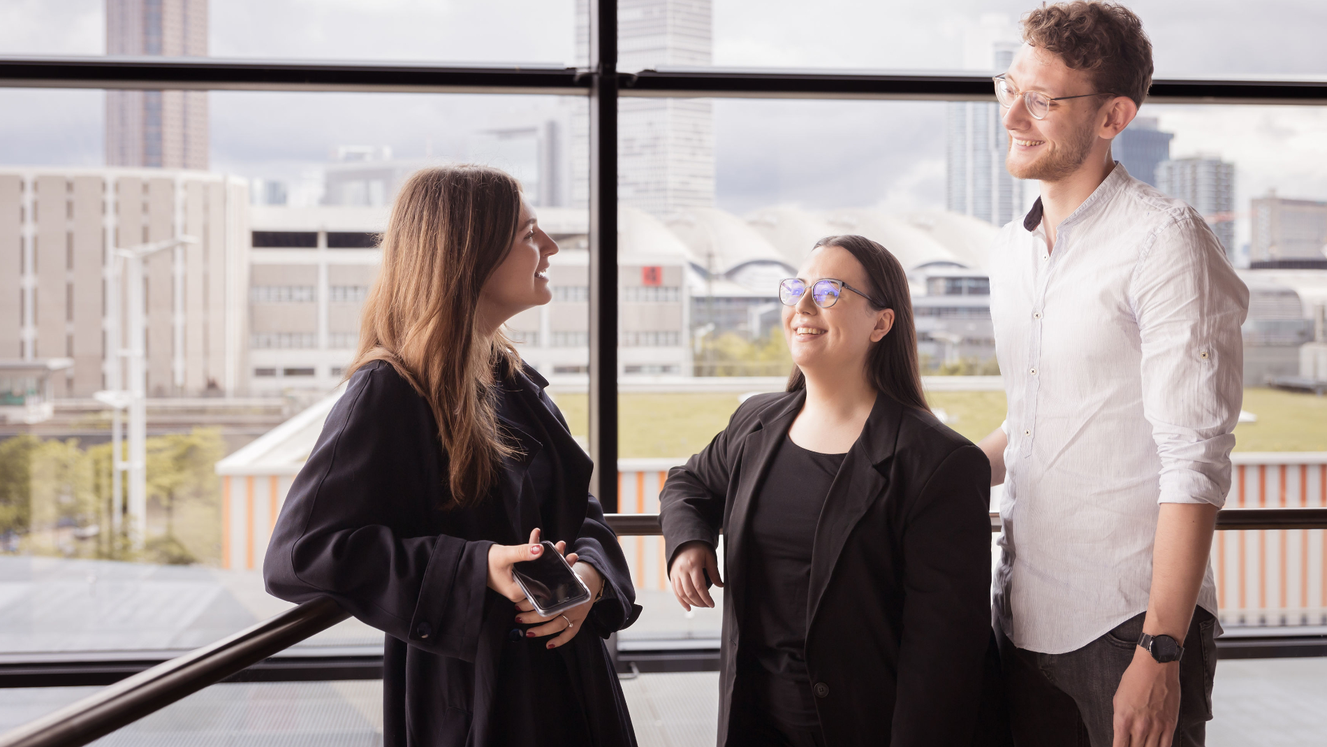 Two young women and a young man talking in front of a window